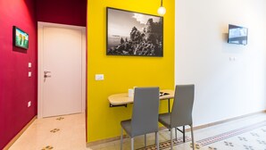 A room with a yellow accent wall, a black and white photograph, a white door, and a small table with two chairs. - Central Station Apts by Wonderful Italy - Capri (Napoli)
