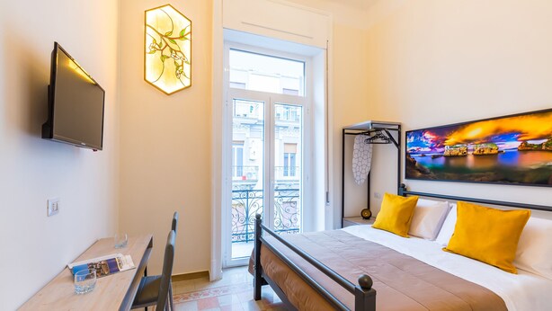 Ein Hotelzimmer mit Bett, Schreibtisch, Stuhl, Fernseher, Fenster und einem Gemälde.