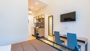 Ein modernes Hotelzimmer mit einem Bett, einem Schreibtisch mit Stuhl, einem Fernseher und einer Küchenzeile.