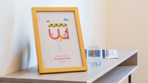 Ein gerahmtes Bild mit einem Cartoon-Zug und Text, auf einer Holzablage zusammen mit einem Glas Wasser und einem Schild.