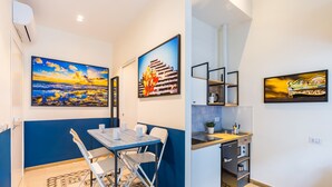 Una habitación compacta con una mesa de comedor, sillas, una kitchenette pequeña y obras de arte en las paredes.