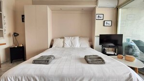A hotel room with a bed, a TV, a small table, and a window with a view. - Studio with seafront terrace (Antibes)