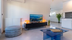 Una sala de estar moderna con un televisor de pantalla plana, una mesa de centro de vidrio y un reposapiés gris.