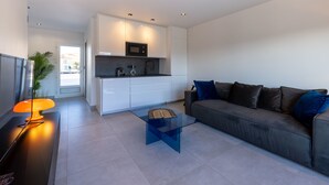 Una sala moderna con un sofá gris, una mesa de centro y una cocina con armarios blancos y un microondas.
