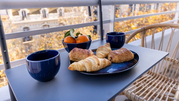 Una mesa en el balcón con croissants, un bol de naranjas y dos tazas azules.