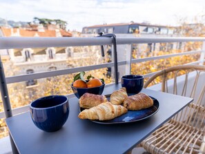 Een balkon met een tafeltje, croissants, een schaal oranjes en twee blauwe bekers.