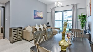 A modern living room with a dining table, beige sofa, and a large window with curtains. - Luxury StayCation - Elegant 1BR Apartment in the Heart of Dubai (Dubai)