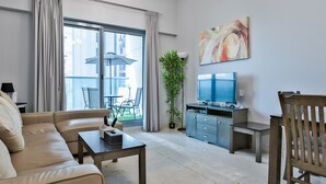 A modern living room with a sofa, coffee table, TV, and a plant. - Luxury StayCation - Elegant 1BR Apartment in the Heart of Dubai (Dubai)