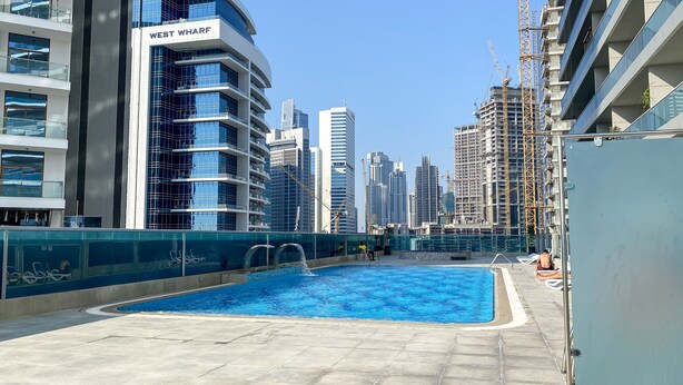 A rooftop pool area with a view of high-rise buildings, including a building labeled "WEST WHARF". - Luxury StayCation - Elegant 1BR Apartment in the Heart of Dubai (Dubai)