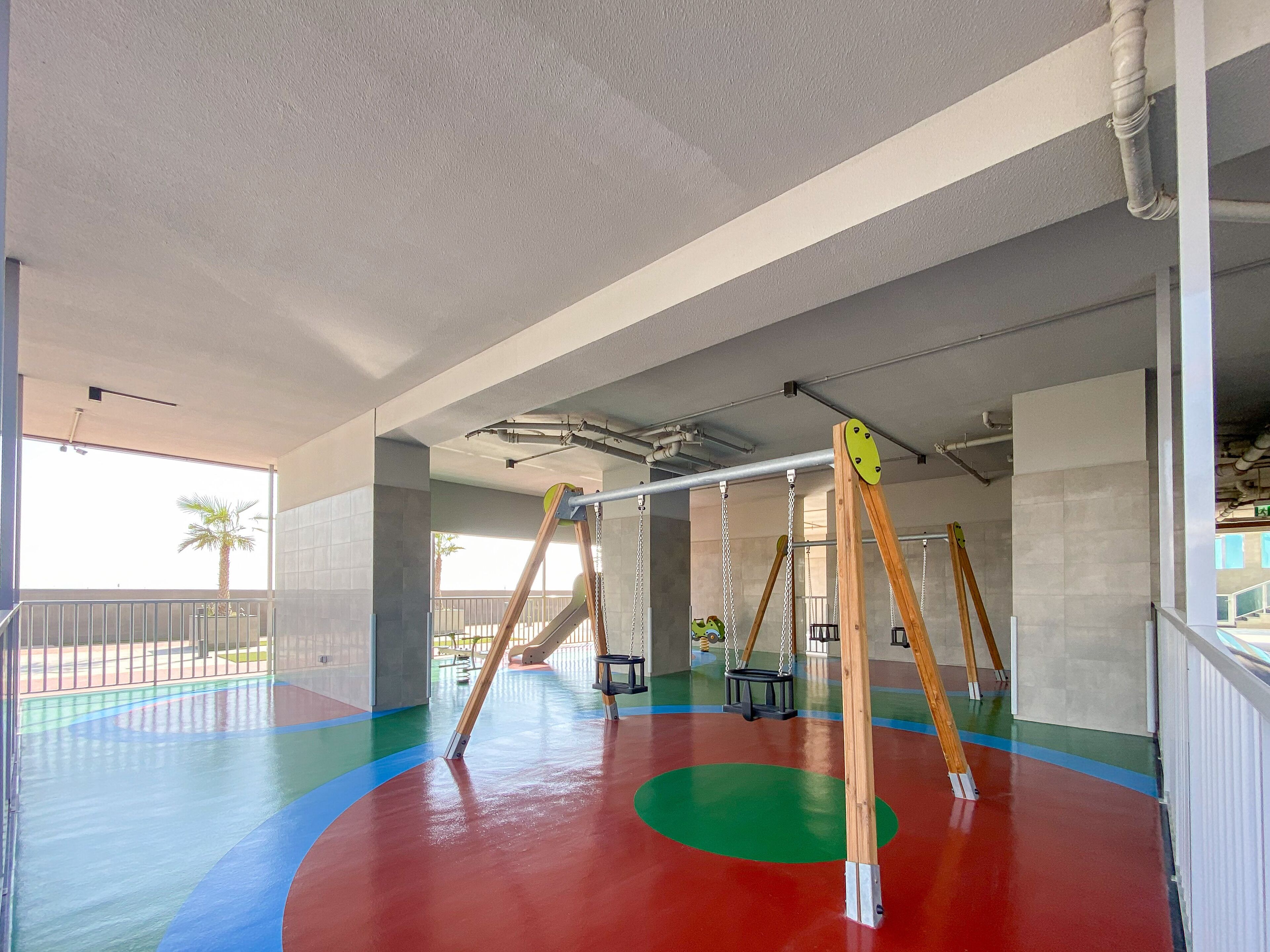 A spacious indoor play area with colorful flooring, swings, and a slide.
