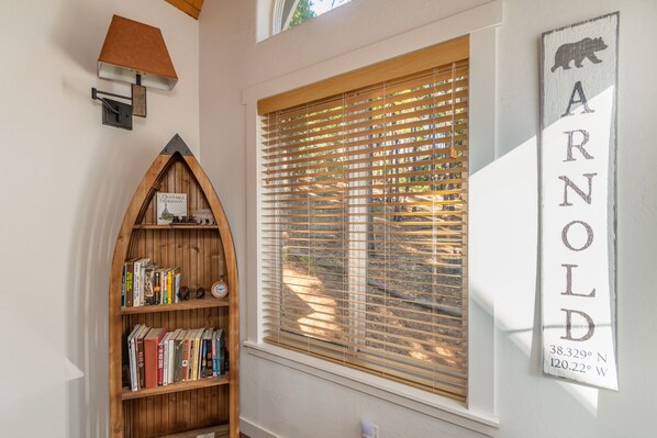 Una habitación con una estantería de madera, una ventana con persianas y un letrero en la pared con coordenadas.
