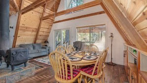 Ein gemütliches Loftzimmer mit Holzbalkendecke, einem Esstisch mit Stühlen, einer Couch und einem Kamin.