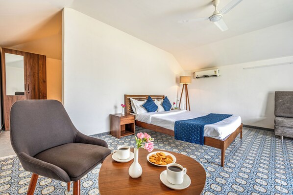 Une chambre d’hôtel avec un lit, une chaise, une table ornée d’un vase de fleurs, une assiette de biscuits et une tasse de café.
