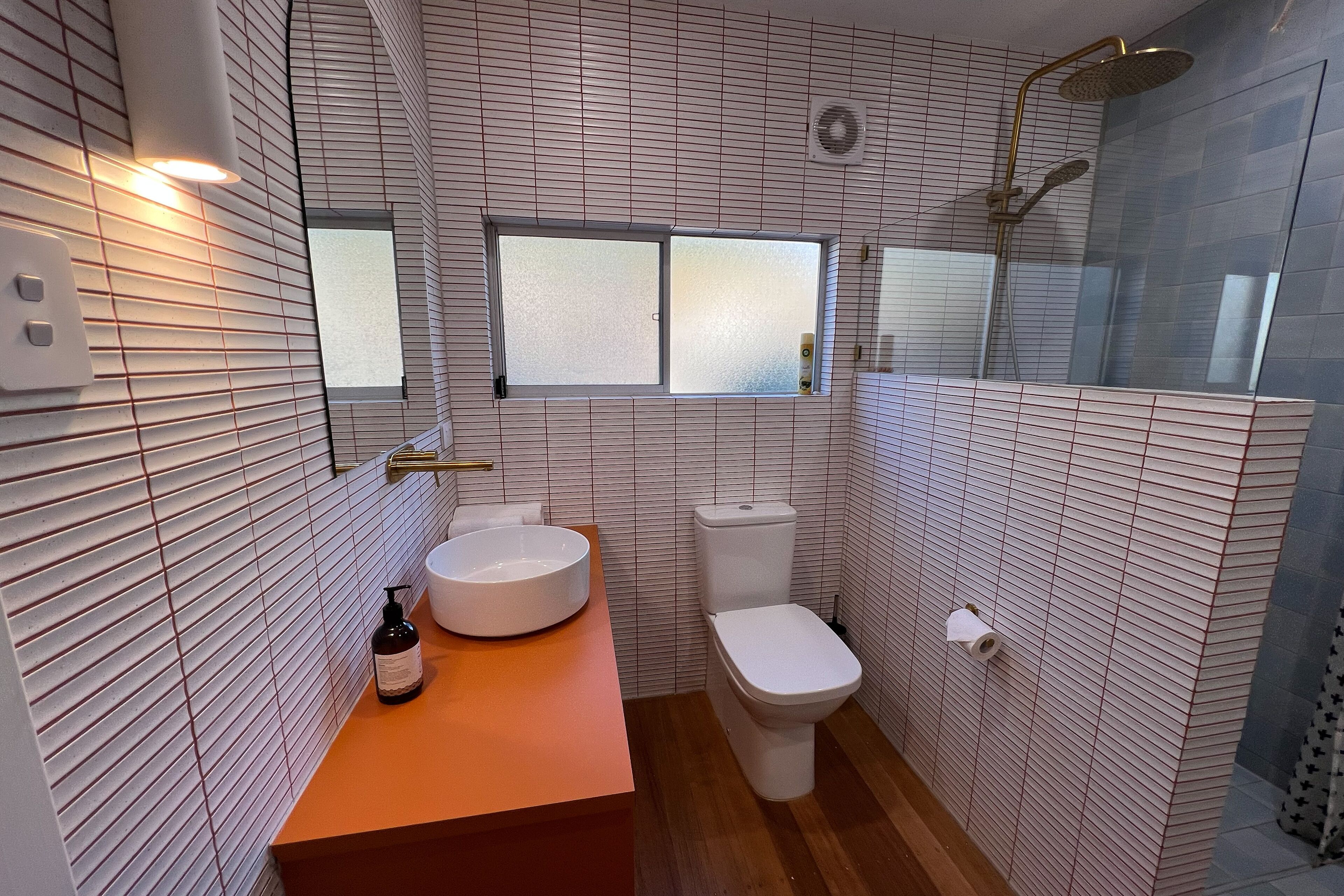 A bathroom with a white tiled wall, a wooden floor, a white sink, a toilet, and a shower area.