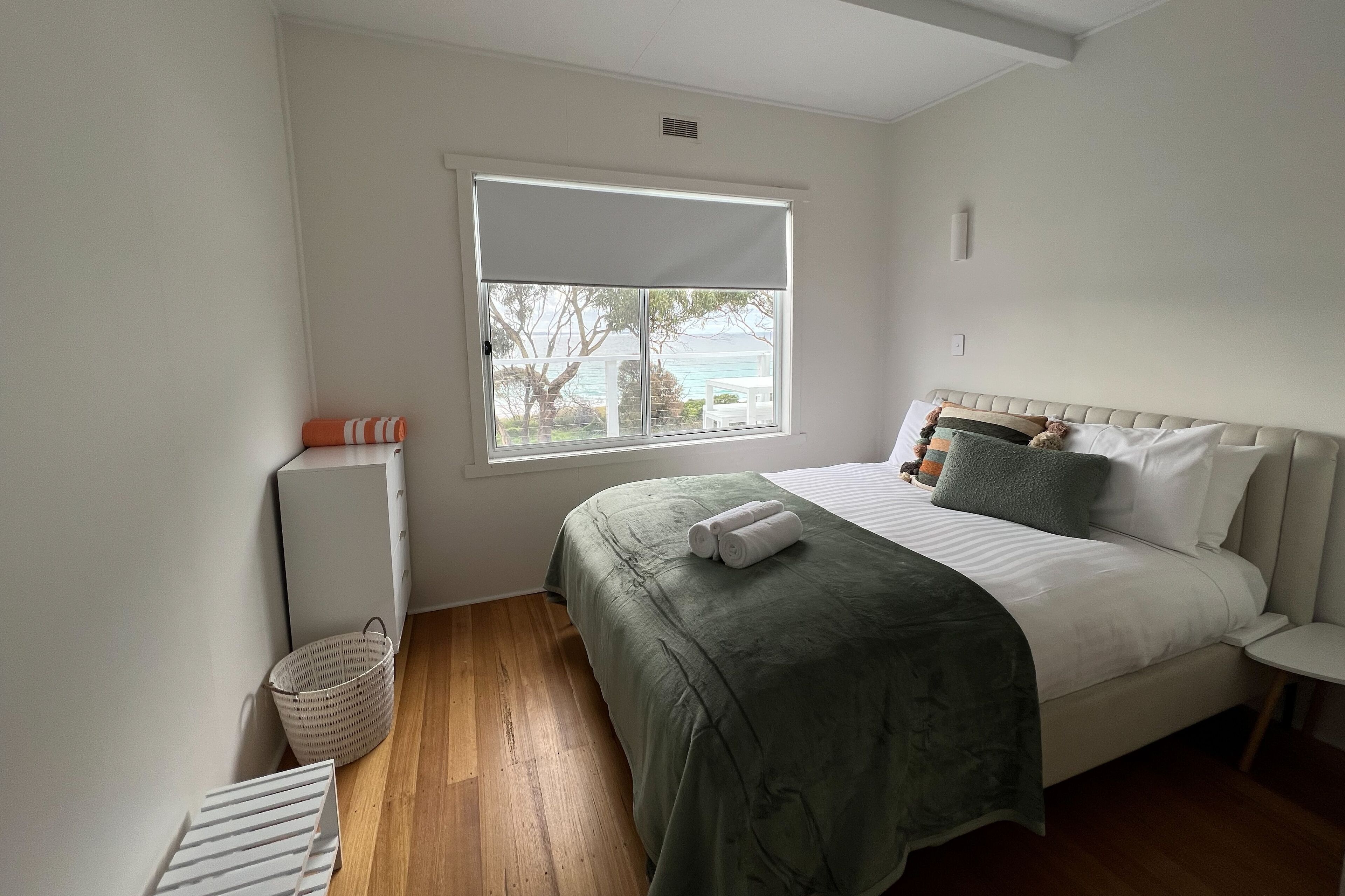 A bedroom with a bed, a window, a bedside table, and a small chair.