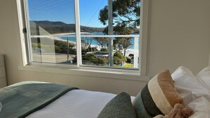 A bedroom with a large window offering a view of a beach and hills. - PIPI SHACK Iconic waterfront shack at Binalong Bay Beach, Bay of Fires (Binalong Bay)