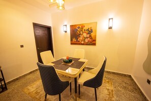 A dining area with a table set for four, a painting on the wall, and a door in the background.