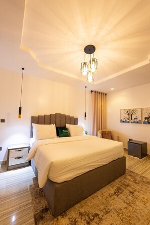 A modern bedroom with a large bed, a headboard, a bedside table, a nightstand, a lamp, and a ceiling light fixture.