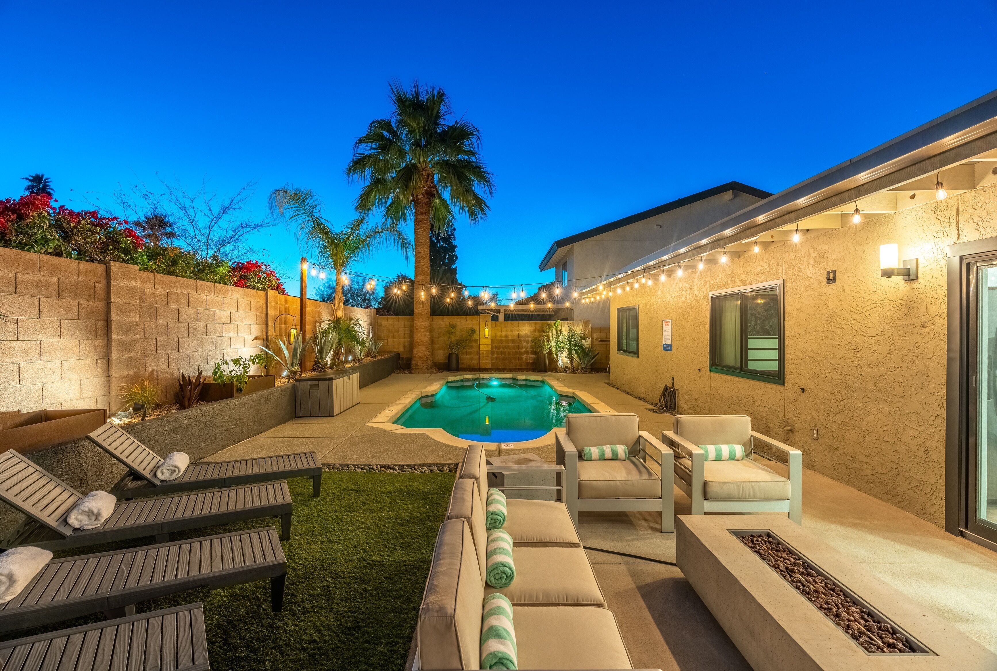 A backyard with a swimming pool, lounge chairs, and a fire pit.