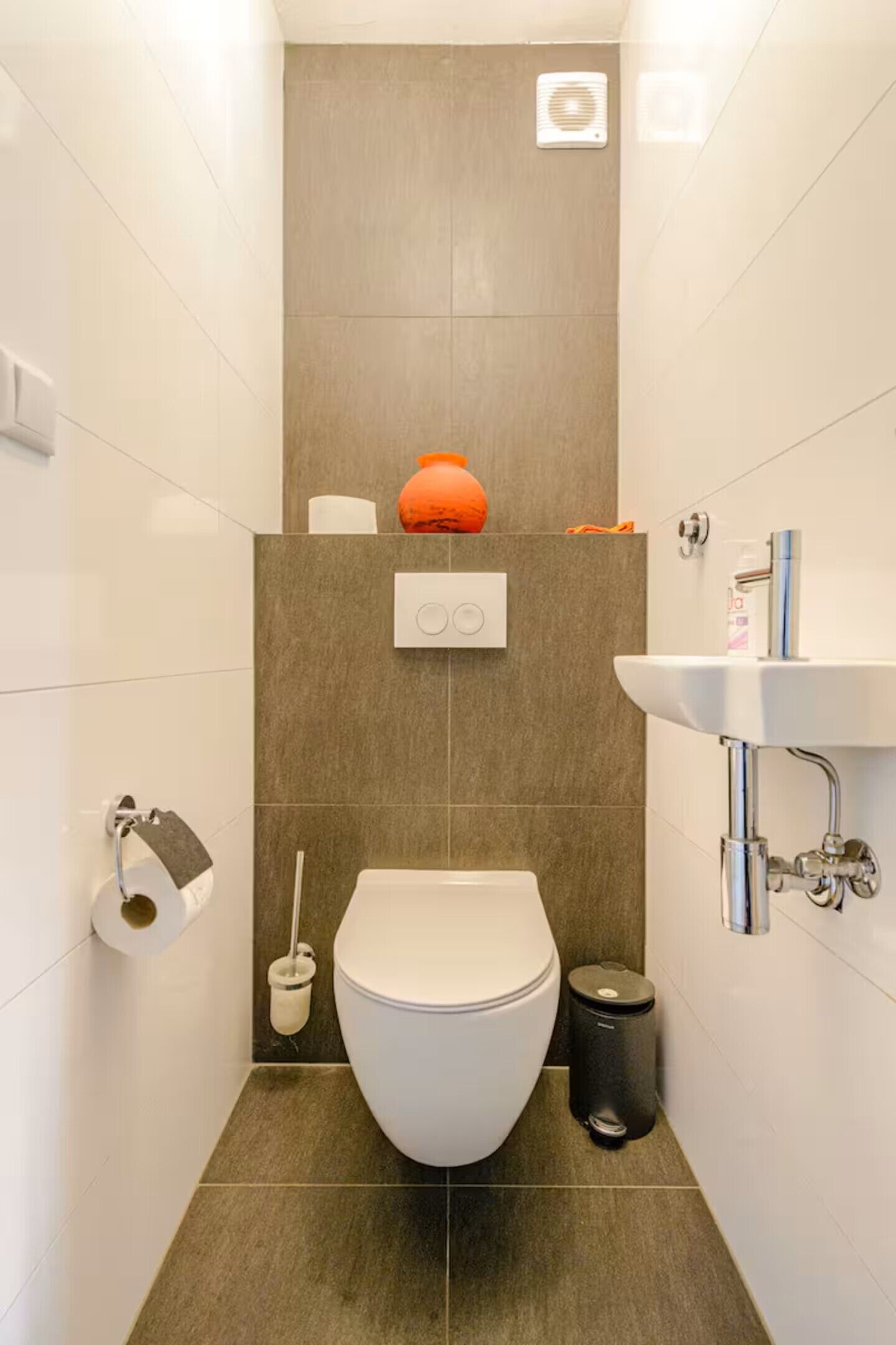 A compact bathroom with a toilet, sink, and a trash bin.