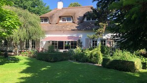 Une maison traditionnelle avec un toit de chaume, une véranda et un jardin bien entretenu.