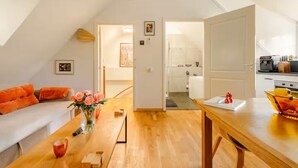 Un appartement moderne avec un espace de vie aménagé en style « loft », une table à manger agrémentée d’un vase de fleurs et une cuisine visible à travers une porte ouverte.
