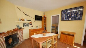 A dining area with a brick fireplace, wooden table, and chairs. There is a television mounted on the wall and a shelf with various items. - SAONA VILLAS (VN ANGEL): villa for 4 people, private pool, wifi, near the sea (L'Ametlla de Mar)