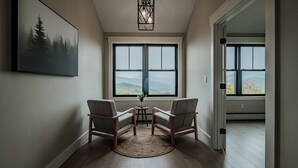 A room with two chairs, a small table, and a view of mountains through large windows. - Panoramic mountain view/Hot Tub/Shuffleboard/Theater room  Sunday River (Newry)