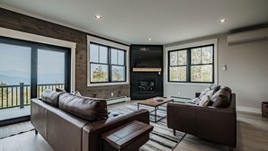 A modern living room with leather sofas, a fireplace, large windows, and a view of the outdoors. - Panoramic mountain view/Hot Tub/Shuffleboard/Theater room  Sunday River (Newry)