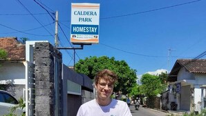 A man on a motorcycle with a sign for Caldera Park Homestay in the background. - CALDERA PARK HOMESTAY SYARIAH (Probolinggo)