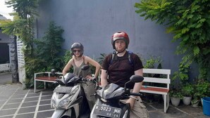 Two people sitting on motorcycles in a courtyard with a bench and potted plants. - CALDERA PARK HOMESTAY SYARIAH (Probolinggo)