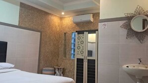 A hotel room with a bed, a small bedside table, a mirror, a sink, and a window with blinds. - CALDERA PARK HOMESTAY SYARIAH (Probolinggo)
