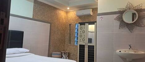 Une chambre d’hôtel avec un lit, une petite table de chevet, un miroir, un lavabo et une fenêtre avec des stores.