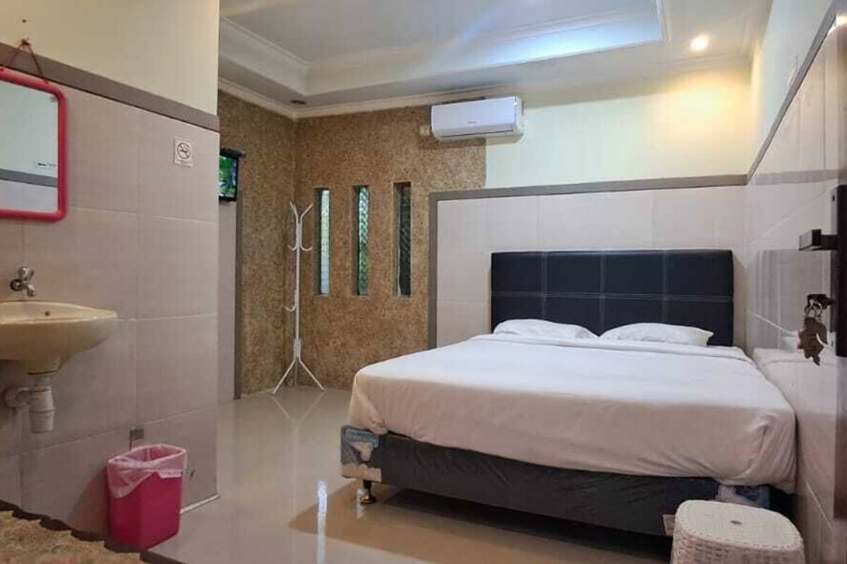 A hotel room with a bed, a sink, a mirror, and a trash bin.