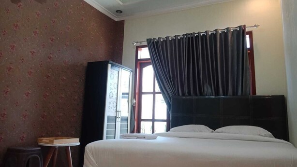 A hotel room with a bed, a small table, a wardrobe, and a window with curtains. - CALDERA PARK HOMESTAY SYARIAH (Probolinggo)