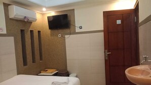 A hotel bathroom with a bed, a sink, a television mounted on the wall, and a wooden door. - CALDERA PARK HOMESTAY SYARIAH (Probolinggo)