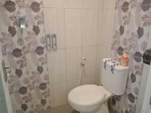 A bathroom with a toilet, a shower, and a toilet paper holder. - CALDERA PARK HOMESTAY SYARIAH (Probolinggo)