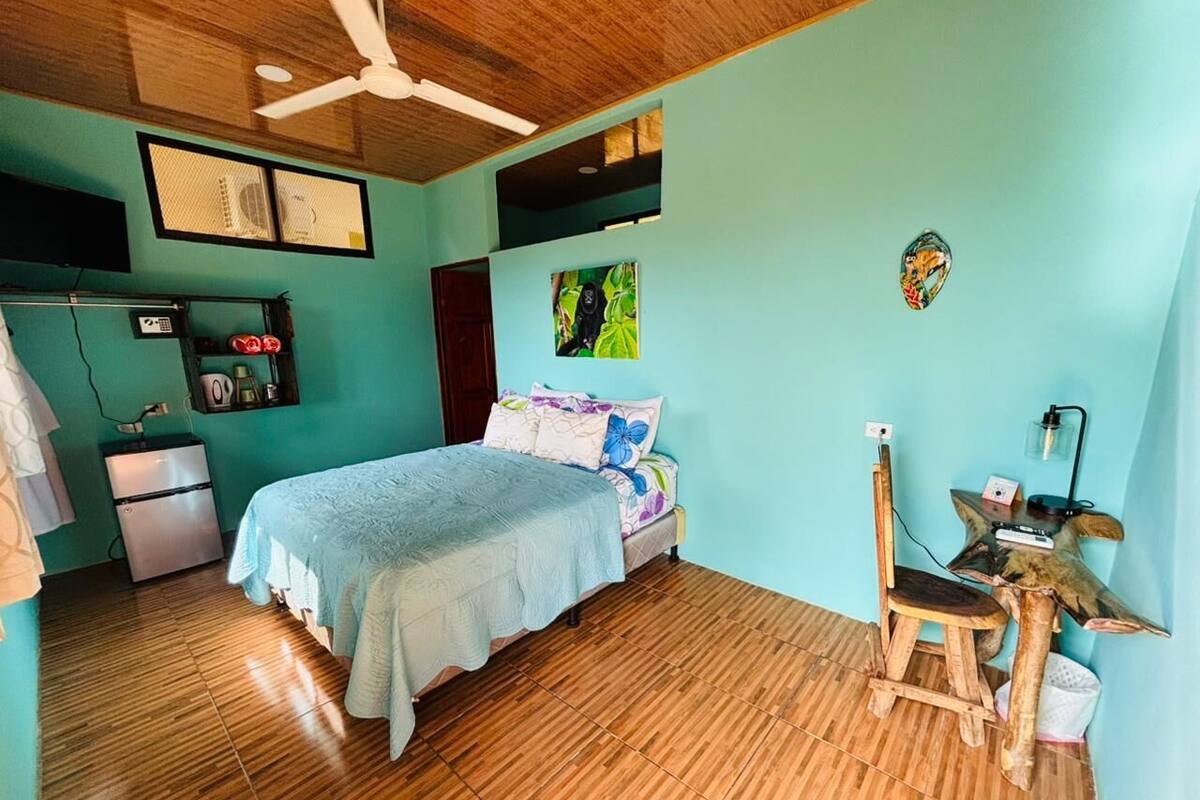 A room with a bed, a desk, a chair, a ceiling fan, and a small refrigerator.