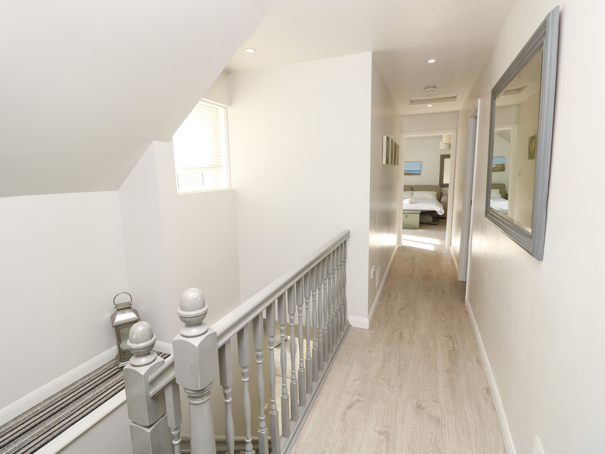 Un couloir doté d’un plancher en bois, de murs blancs et d’un escalier avec une rampe blanche.