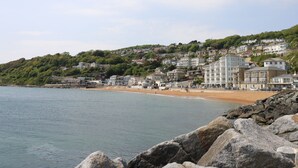 A coastal town with a beach, rocky shoreline, and hillside buildings. - Burwyns (Ventnor)