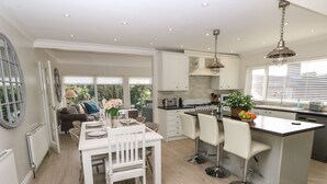A modern kitchen with white cabinetry, a dining area with a white table and chairs, and a large window providing natural light. - Burwyns (Ventnor)