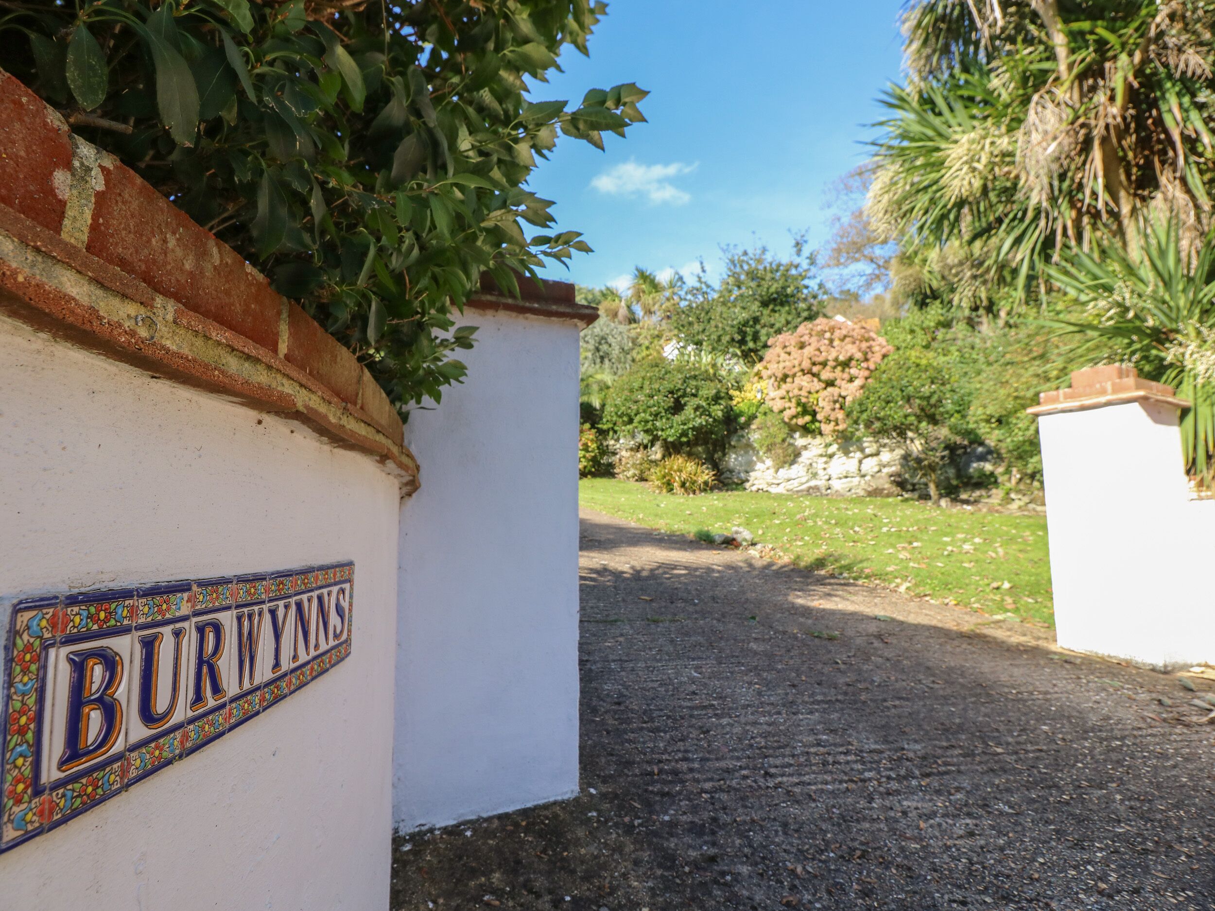 Eine weiße Wand mit einem farbenfrohen Schild mit der Aufschrift "BURWYNNS" und einem Kopfsteinpflasterweg, der durch einen Garten führt.