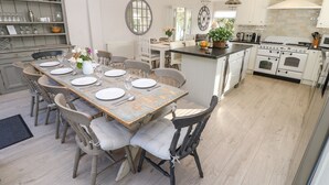 A spacious kitchen with a central island, white cabinetry, and a dining area with a rustic wooden table and chairs. - Burwyns (Ventnor)