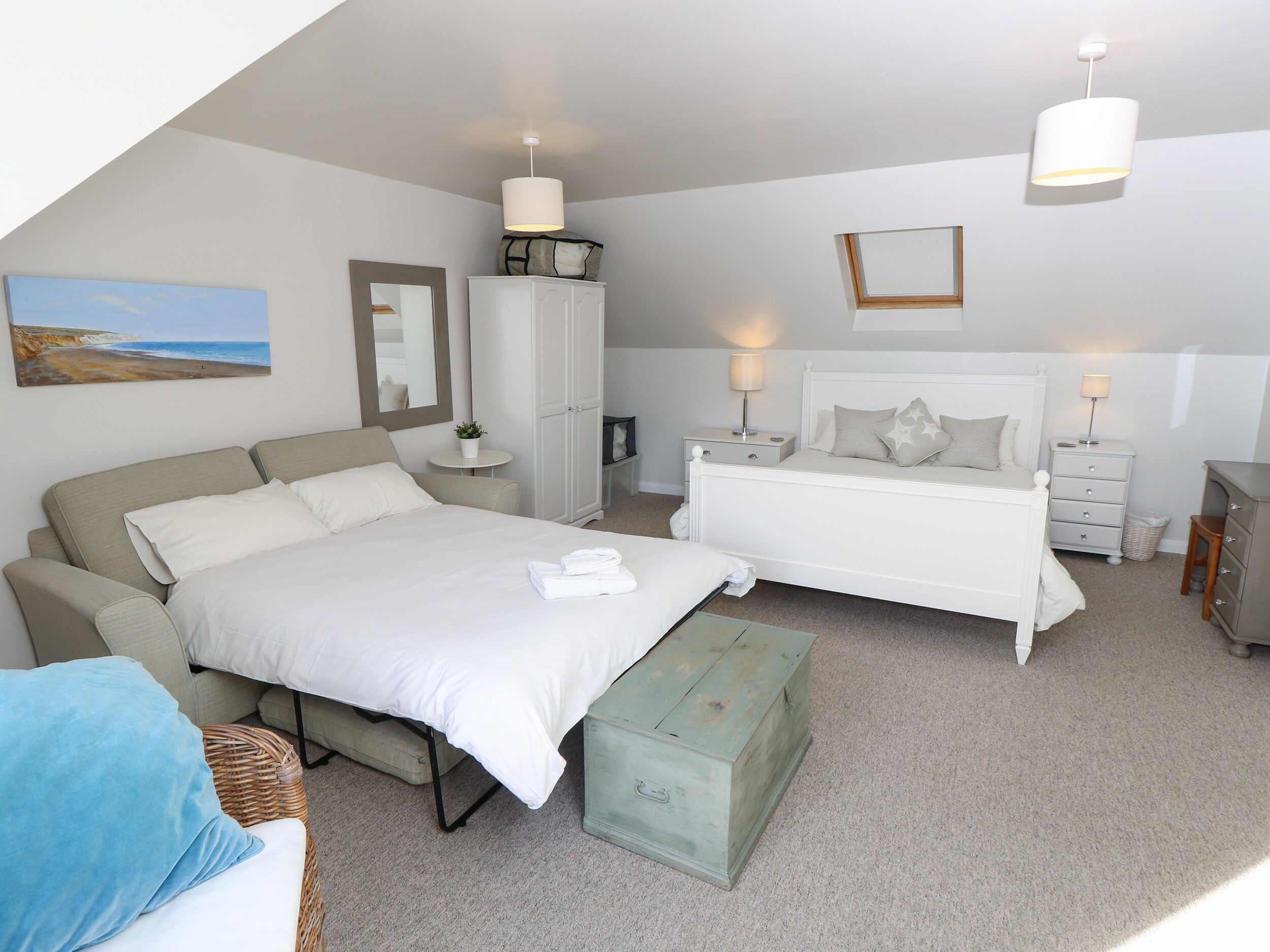 A bedroom with a large bed, a smaller bed, a wardrobe, a bedside table, a lamp, a mirror, and a painting on the wall.