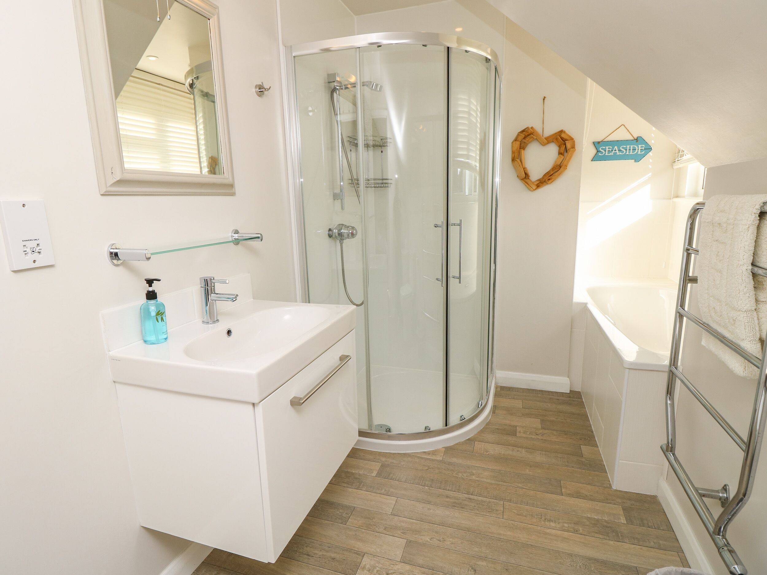 Une salle de bain moderne avec une douche à parois de verre, un lavabo blanc doté d’un distributeur de savon et une baignoire avec un porte-serviettes.