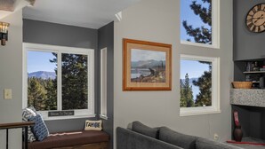 A living room with a view of a lake and mountains, a sofa, a bench, and a clock on the wall. - Carnelian Woods # 126 by Hauserman Rental Group (Carnelian Bay)