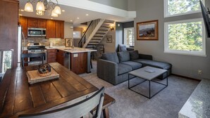 A modern kitchen with wooden cabinets, a central island, and a dining area with a wooden table and chairs. - Carnelian Woods # 126 by Hauserman Rental Group (Carnelian Bay)