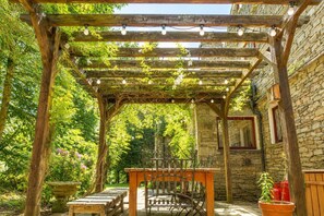 A wooden pergola with string lights, a stone wall, and a table with chairs.