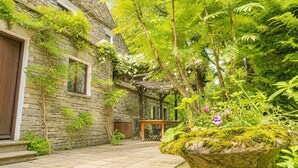A stone building with a wooden door, a stone wall, and a garden with a wooden table and chairs. - Daweswood, Patterdale luxurious, spacious home with walks from the door (Patterdale)