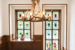 A chandelier made of antlers, stained glass windows with geometric patterns, and a metal pitcher on a wooden ledge.
